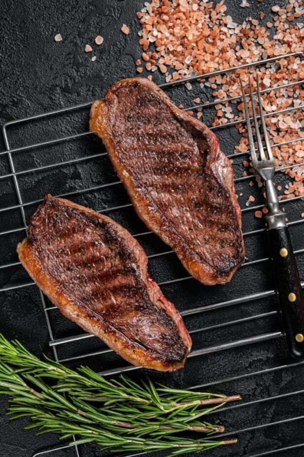 BBQ Grilled cap rump or Top sirloin beef steak, fried meat on grill. Black background. Top view